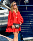 Woman in red dress wearing a black clutch with colorful butterfly print.