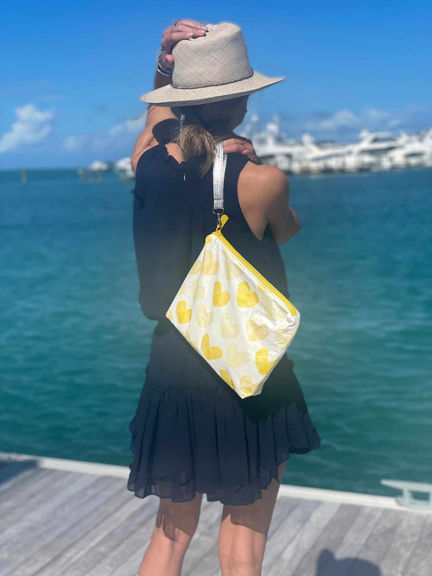Woman wearing black holding yellow heart bag by the water