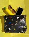 Black pouch with colorful butterflies holding sunblock, sunglasses, and cell phone on yellow background