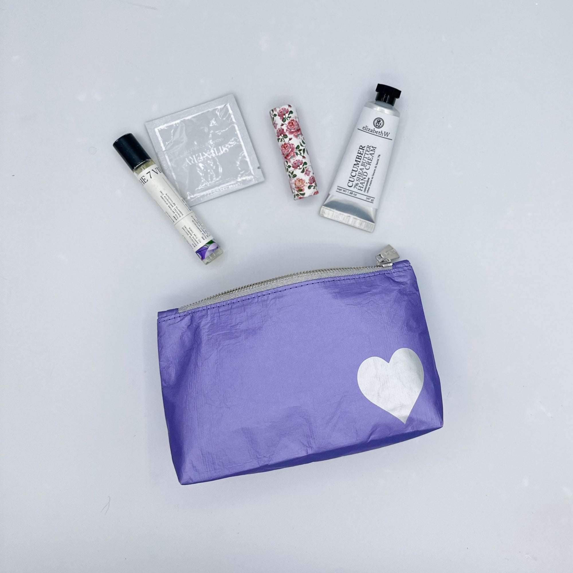 mini pouch in purple with silver heart with lip balm, hand lotion, perfume on white background