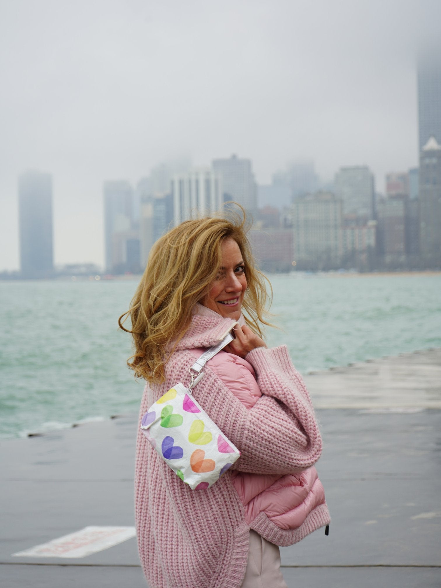woman in front of Chicago skyline holding a rainbow heart zipper pouch wristlet