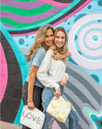 Women against graffiti wall holding yellow pouch with hearts and white pouch with LOVE