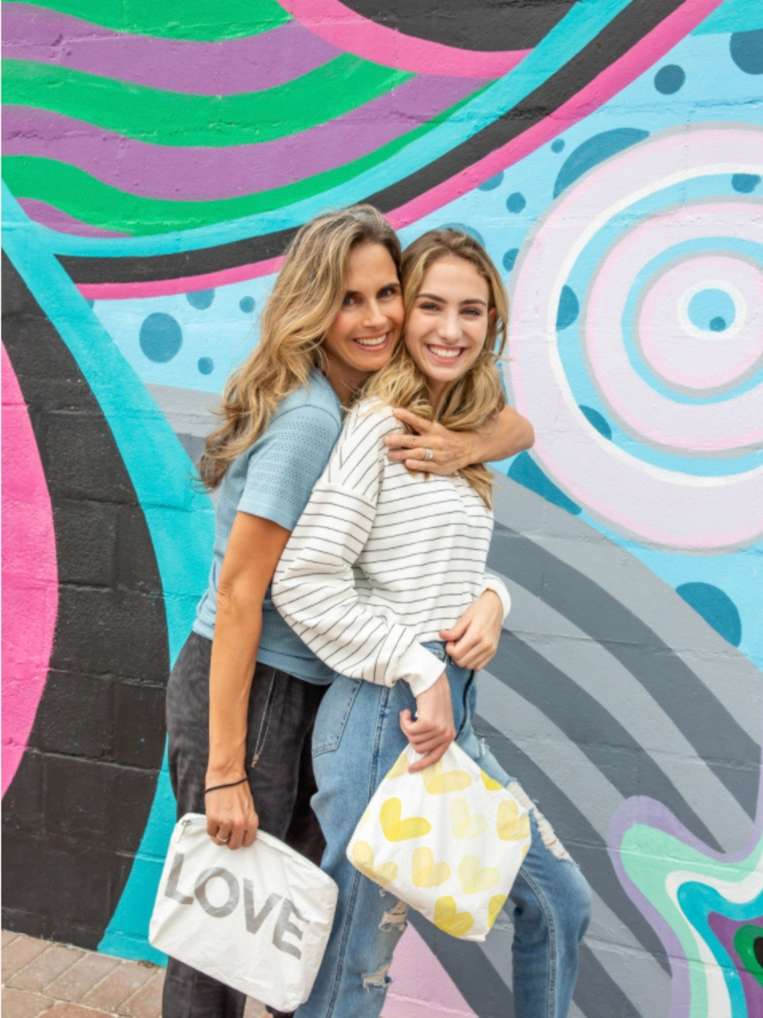 Women holding yellow heart pouch and white LOVE pouch against graffiti wall