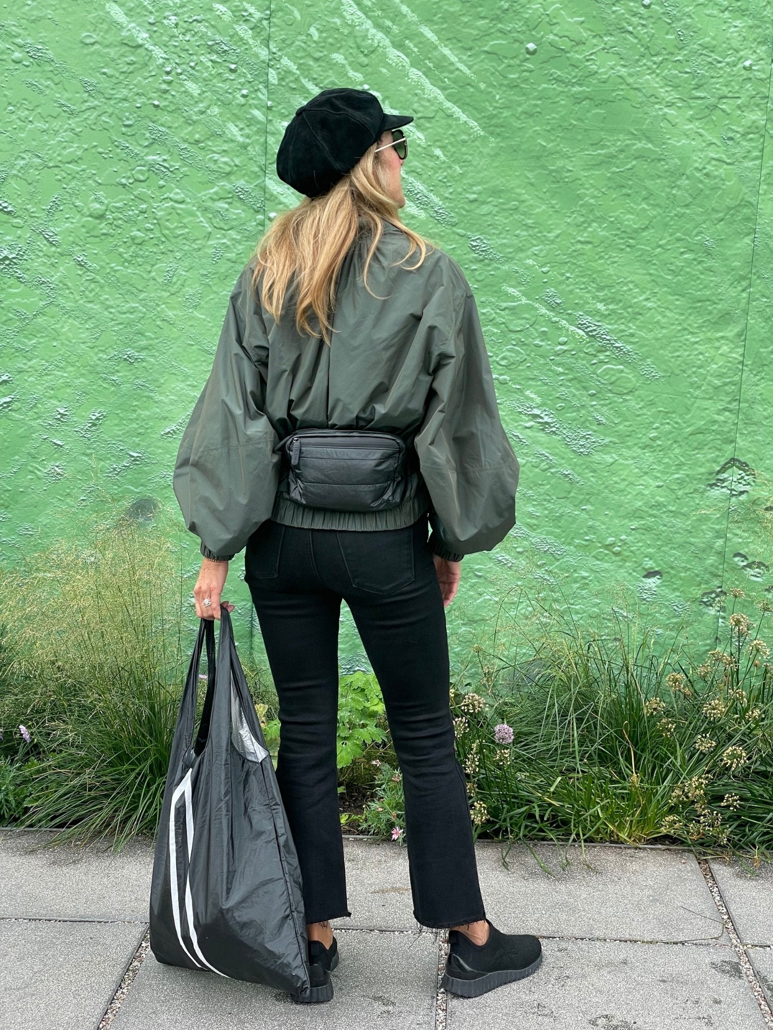 Woman standing in front of green wall wearing Puffer Crossbody Fanny Pack Belt Bag in Shimmer Black