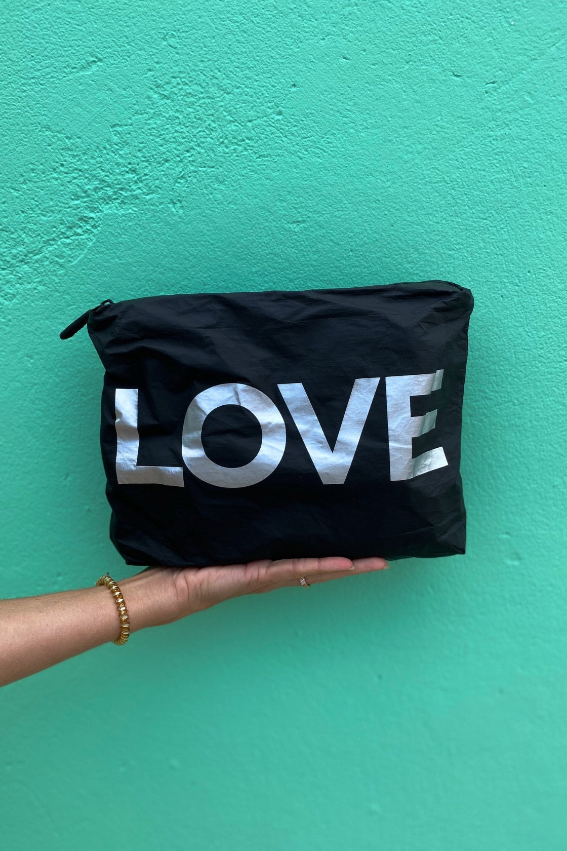 Hand holding the Medium Pouch in Black with Silver LOVE against a bright teal wall