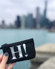 Hand holding the black H! Card Pouch with a city skyline and water in the background
