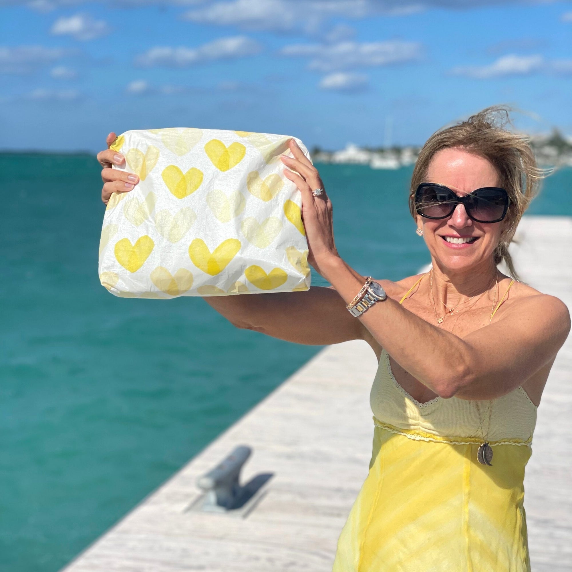 Woman wearing yellow dress holding yellow heart pouch by water