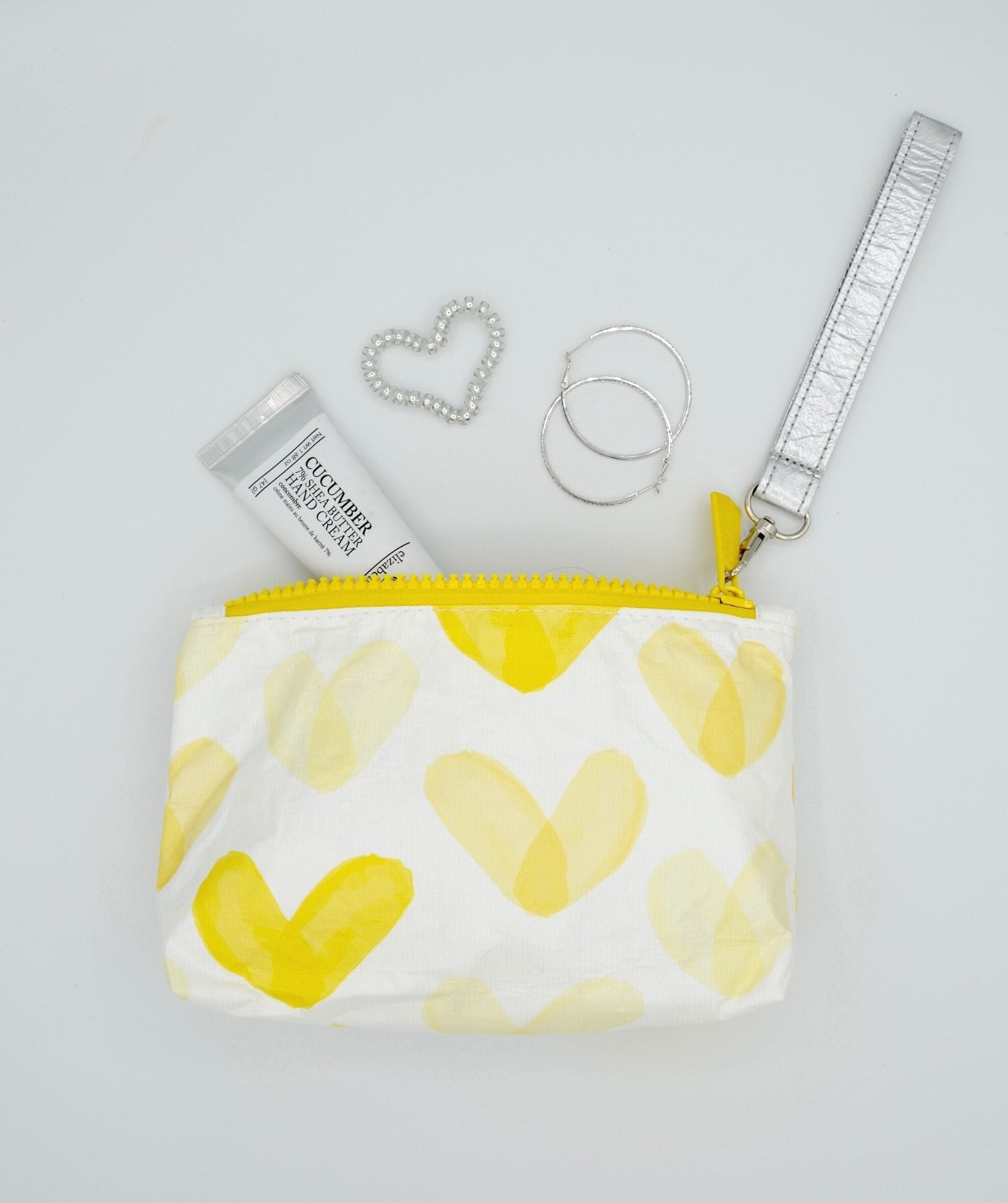 Yellow heart wristlet with earrings and hand cream on white background