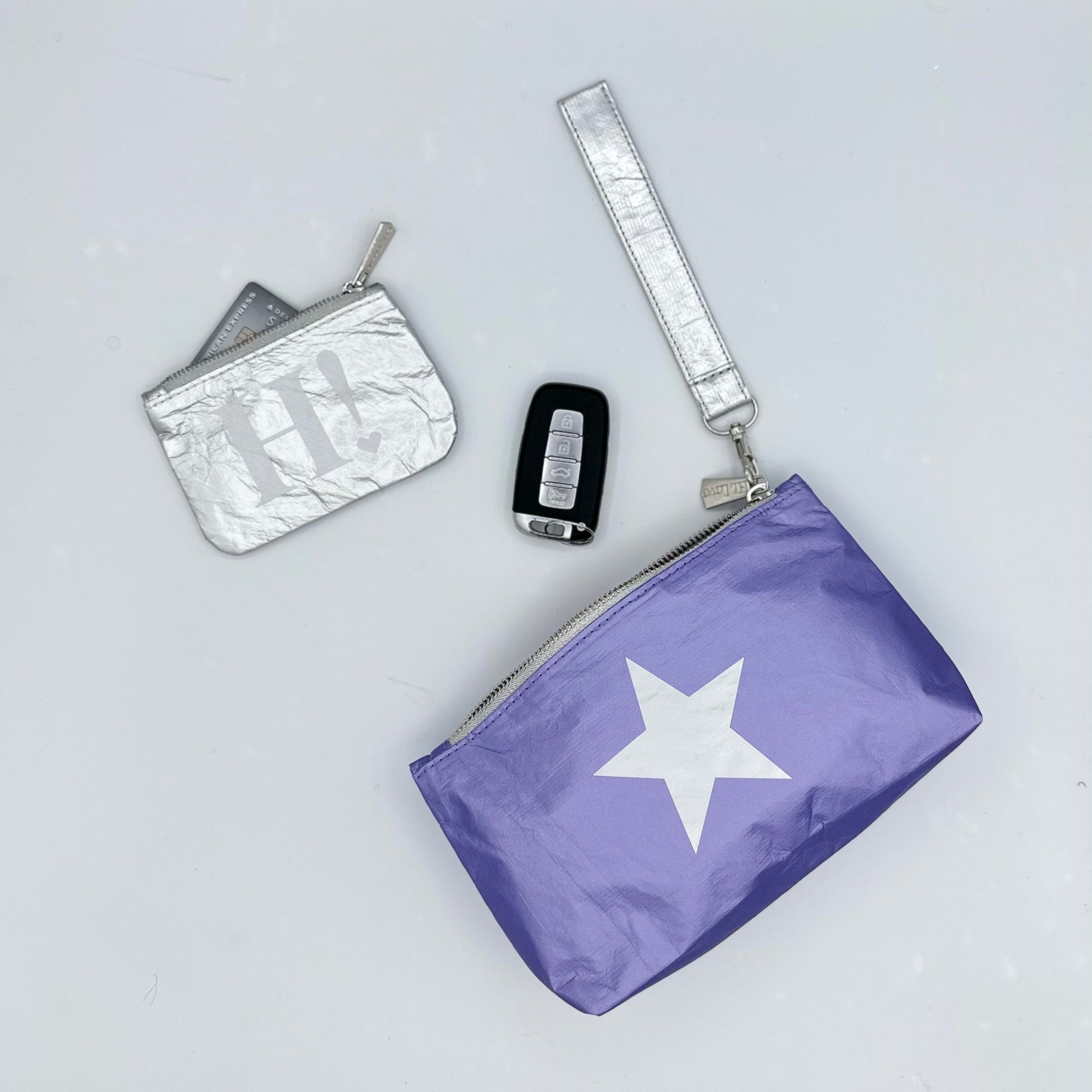 Purple wristlet with silver star, card pouch, and car keys on white background