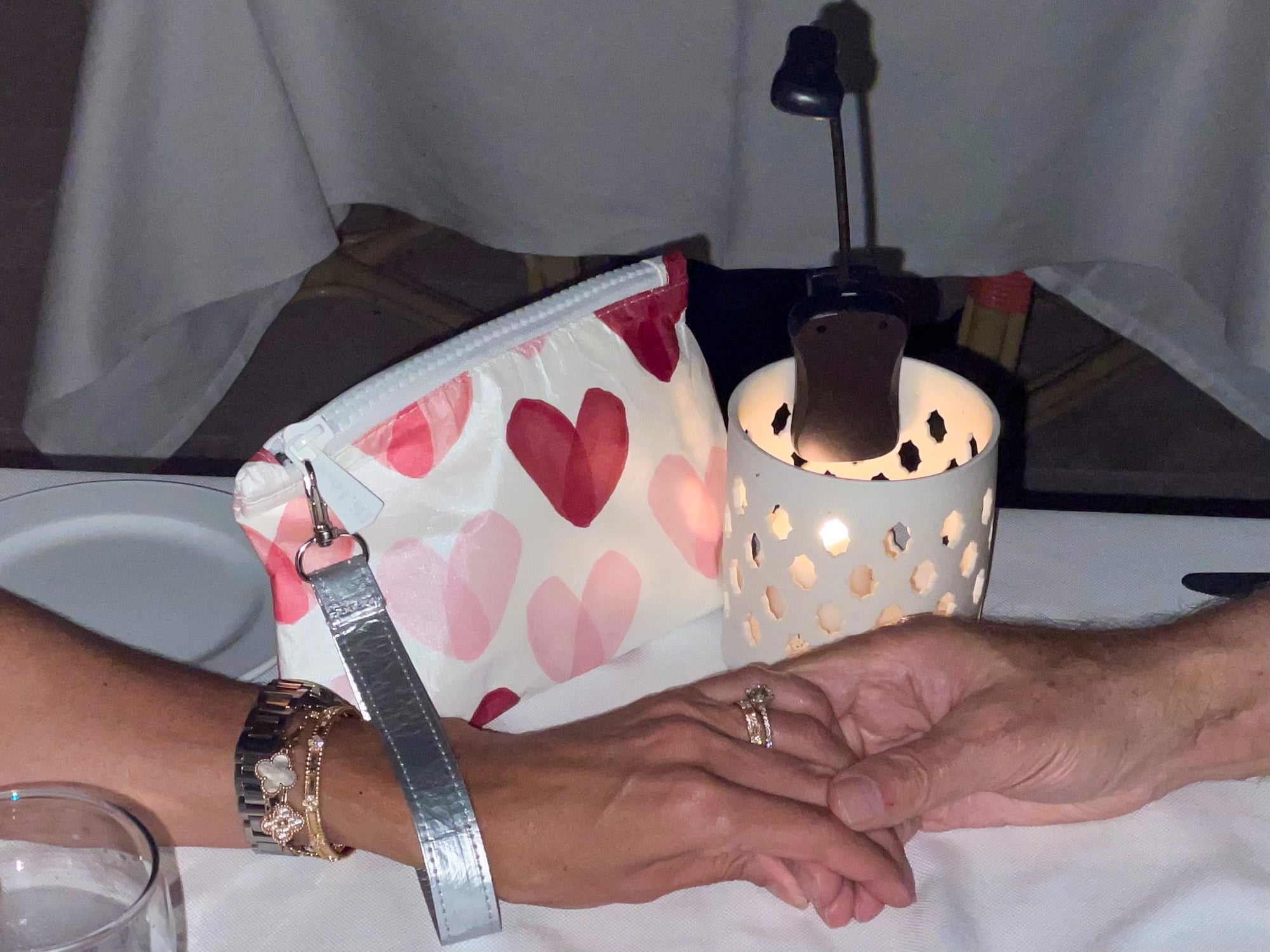 Couple holding hands wearing mini  zipper pouch with detachable wristlet strap in multicolored heart print