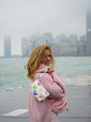 woman holding rainbow hearts zip wristlet in front of chicago skyline
