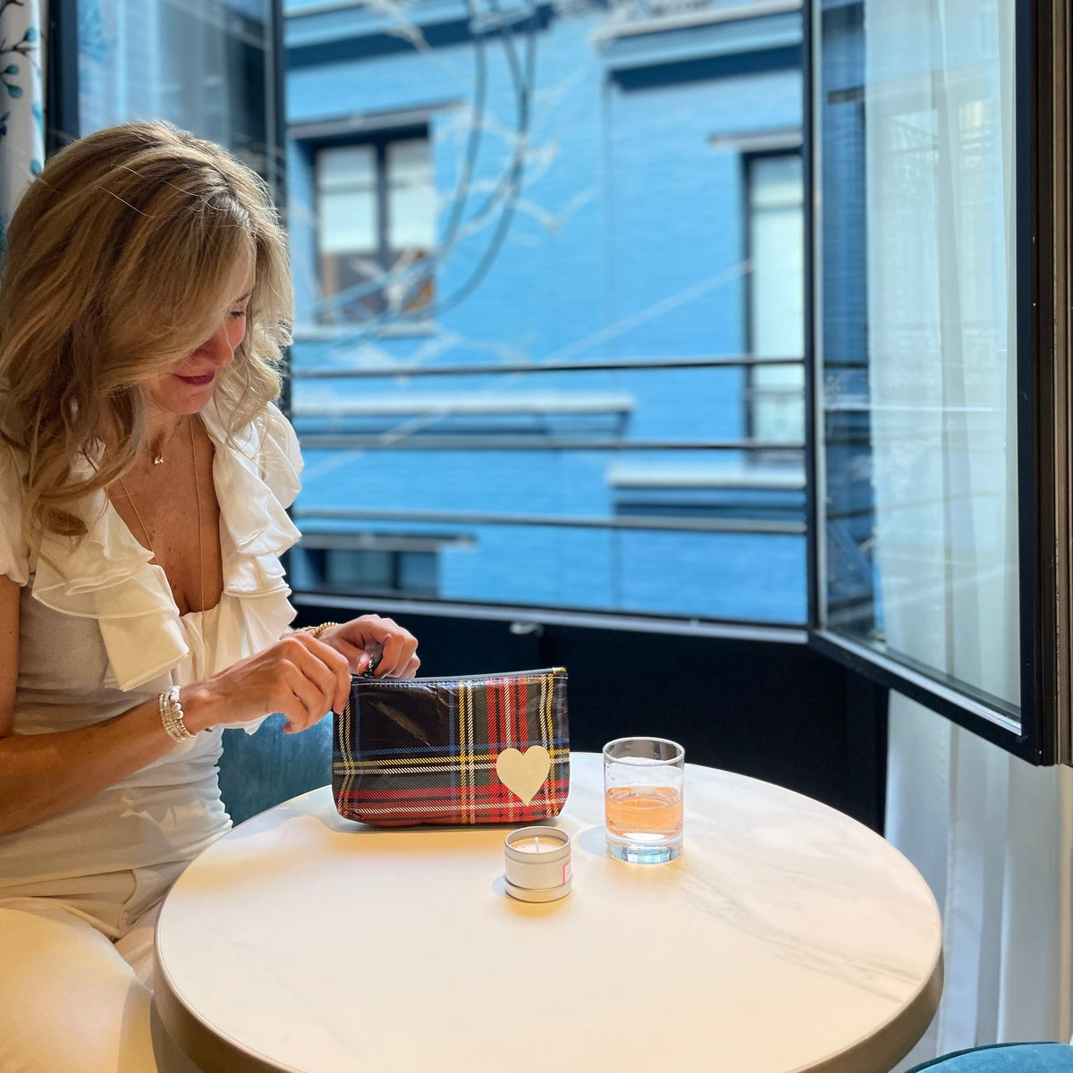 Woman sitting at table using mini zipper pack in tartan plaid with a white heart against window background